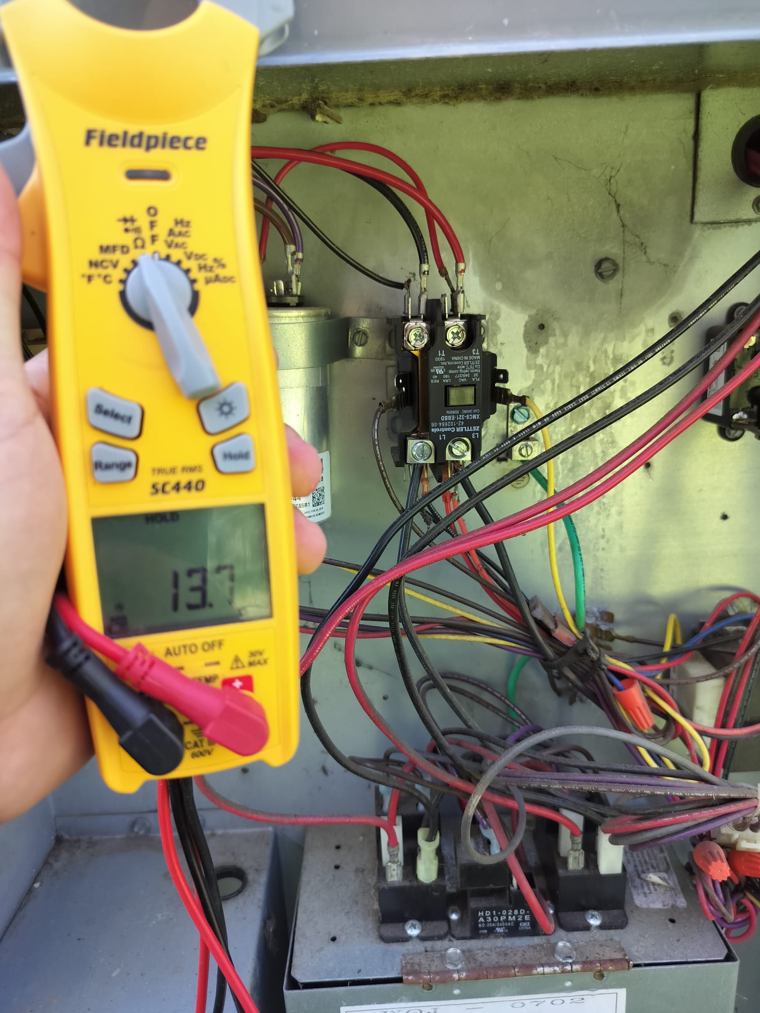 Technician using a multimeter inside an HVAC control panel