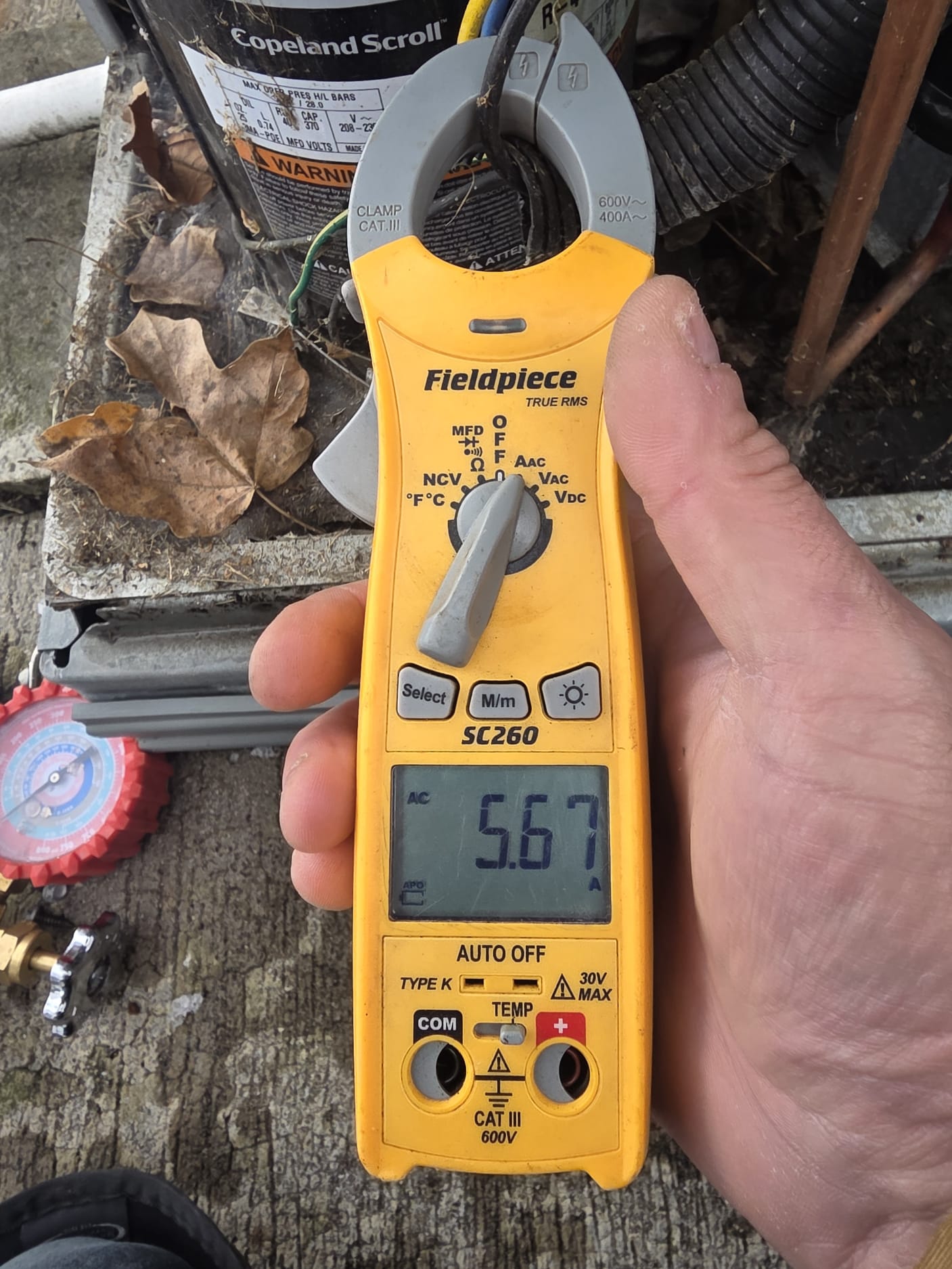 Technician using clamp meter to measure current on HVAC compressor