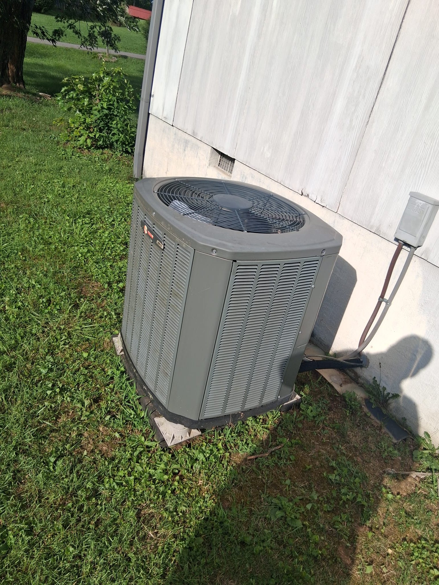 The image shows an outdoor HVAC condenser/heat pump unit installed next to the exterior wall of a home.
