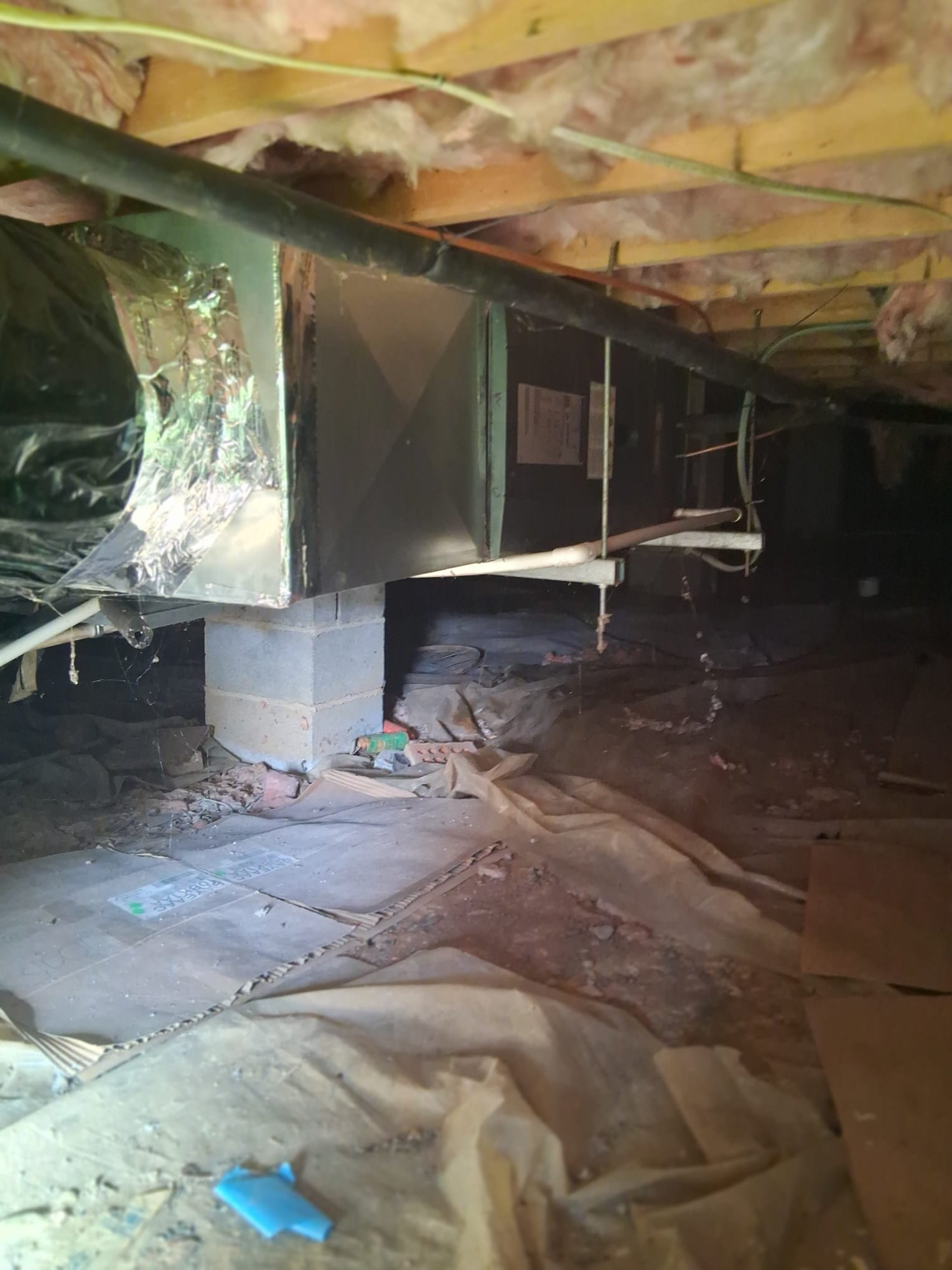 The image shows an HVAC air handler or furnace unit installed in a low crawl space.